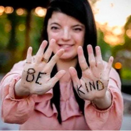 Image Description: Rena Rosa holds up her hands to the camera. Written on them are the words: "Be Kind." 