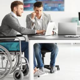 two men sitting at a table, one in a wheelchair, both working on a project
